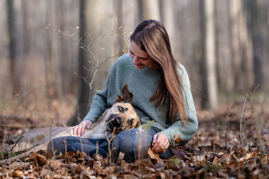 Mensch-Tierfotografie. Ein Hund liegt im Schoß seines Frauchens im Wald.